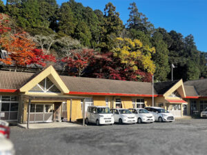 秋の紅葉を背景にした介護施設の建物外観と駐車場